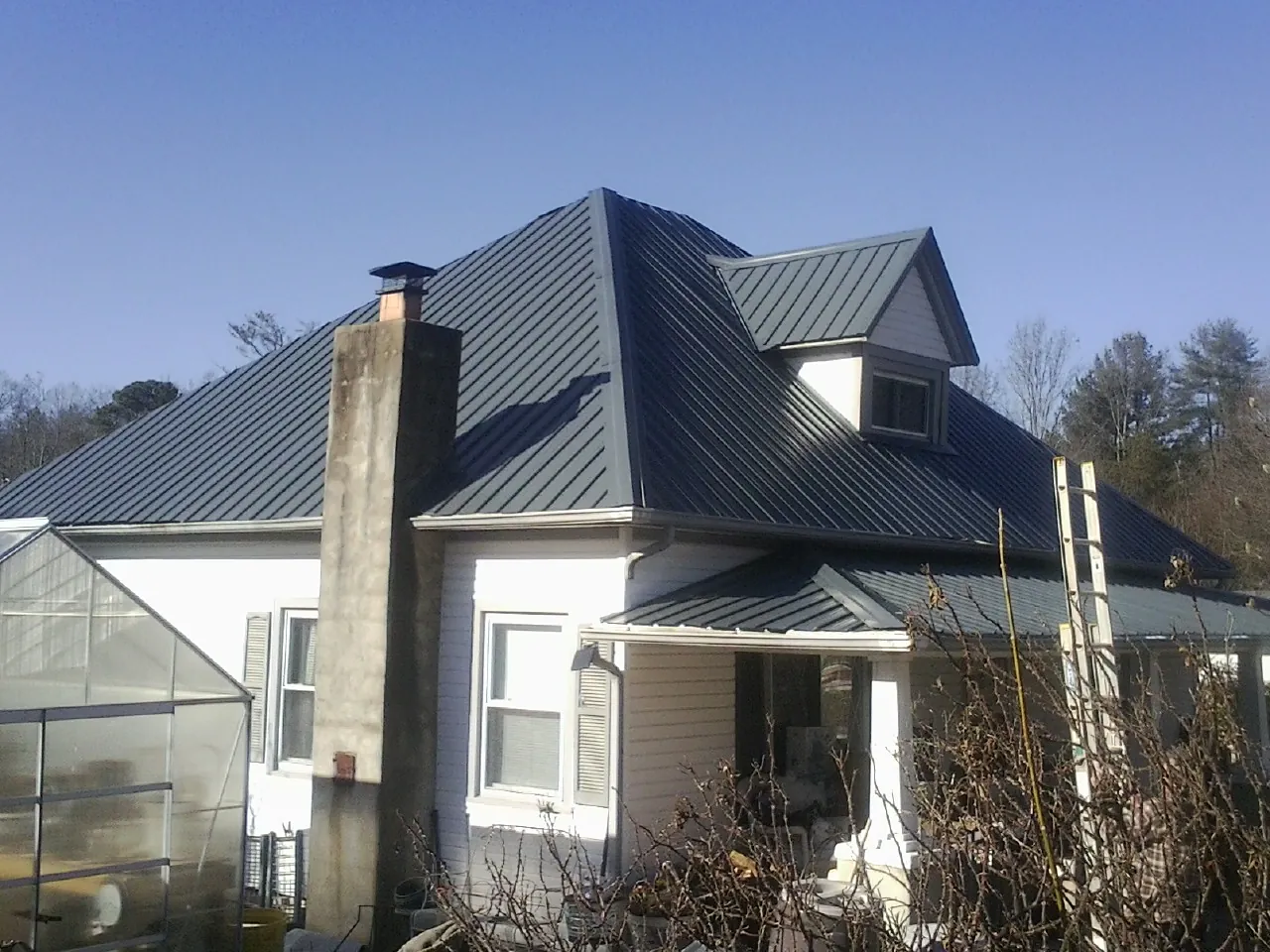 Dark blue standing seam metal roof on a white farmhouse with dormer — Slate & Tile Roof Repair by Roofing Brothers in Great Meadows