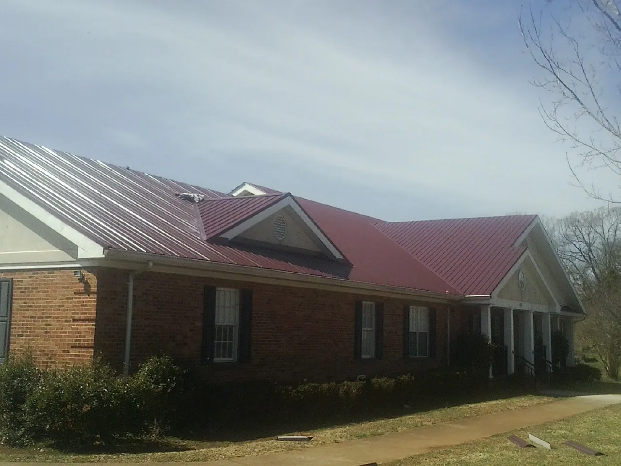 Red metal roof with gabled entries on a long brick building, from a Hail Damage Roof Repair job in Great Meadows