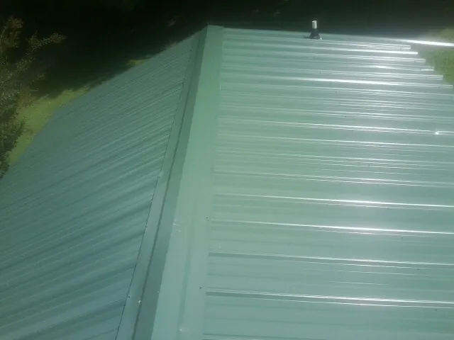 New green metal panels meeting at the ridge of a roof — Flat Roof Repair work by our crew in Great Meadows