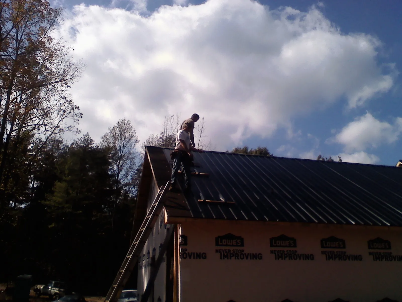 Roofer fastening dark metal panels high against a cloudy sky, from a Roof Inspection job in Great Meadows