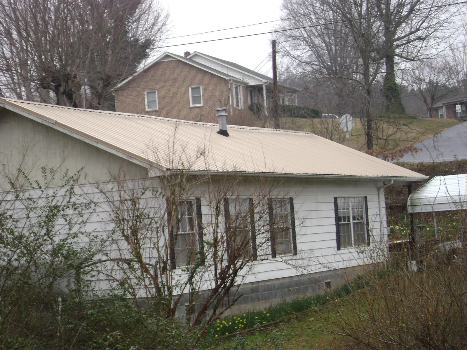 Tan metal roof on a white sided house set into a hillside — Commercial Roofing by Roofing Brothers in Great Meadows