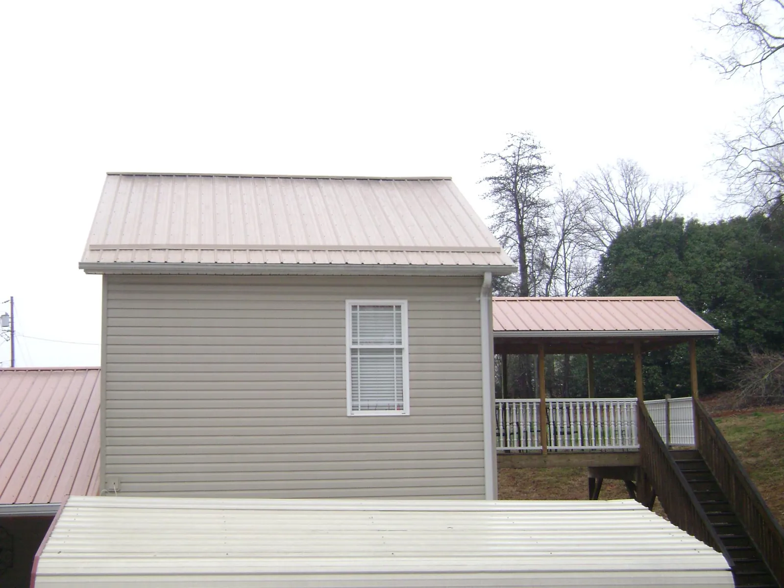 Tan metal roofs on a two story addition and attached porch, from a Roof Replacement job in Great Meadows